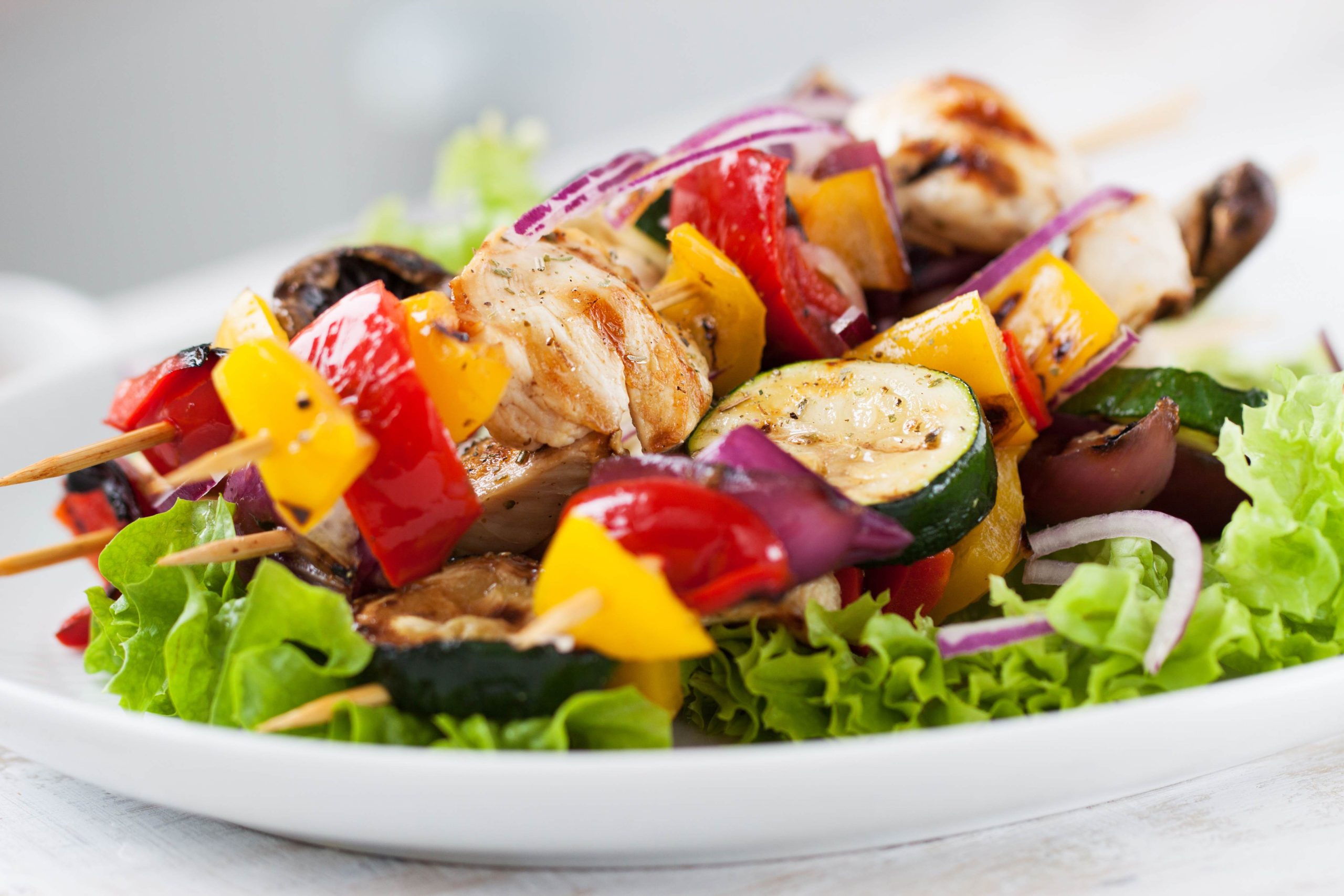 Closeup of chicken skewers or shashlik with grilled vegetables (mushrooms, paprika, salad, zucchini, onion)